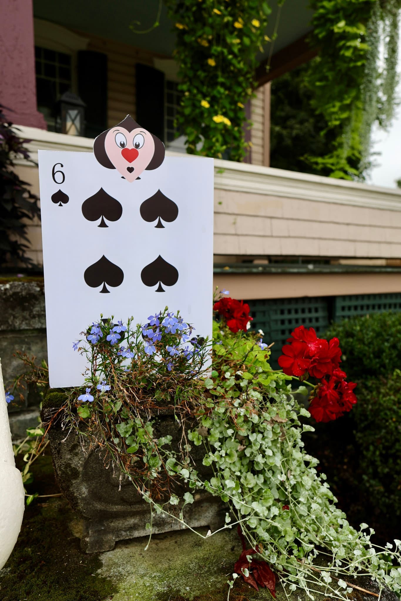 Giant Six of Spades card soldier in a planter with red geraniums