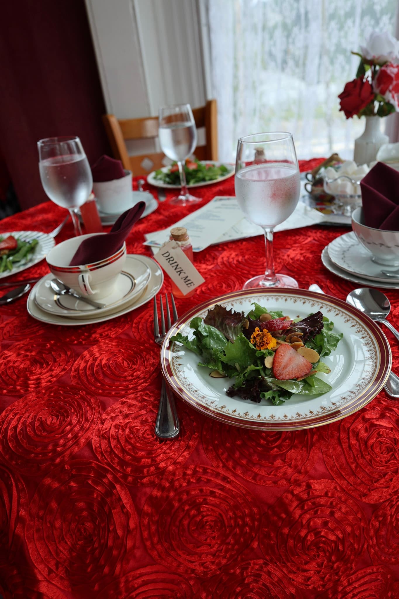 Drink Me vial and garden salad on a red rose tablecloth in the Red Queen Room
